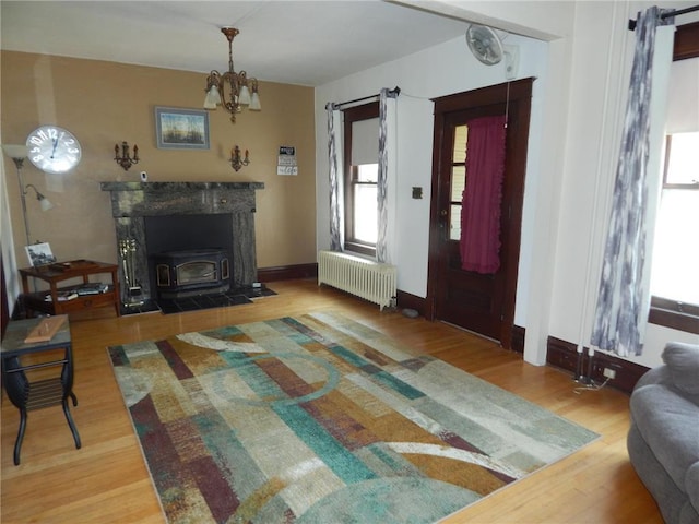 living area with radiator heating unit, a wood stove, wood finished floors, a chandelier, and baseboards
