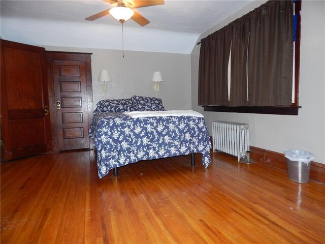 bedroom with radiator, wood finished floors, vaulted ceiling, and a ceiling fan