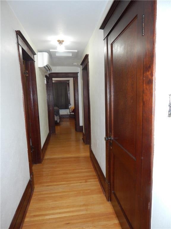 hall with light wood-style flooring, baseboards, and attic access