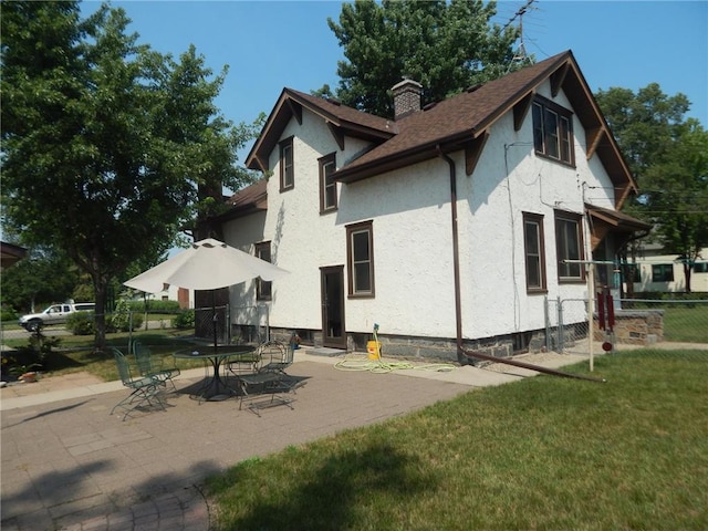 back of house with stucco siding, a chimney, a patio area, and roof with shingles