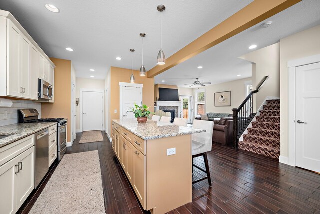 1013 Planters Path, Bayport, MN 55003 - kitchen featuring stainless steel appliances, a fireplace, a kitchen breakfast bar, ceiling fan, and dark wood-style floors