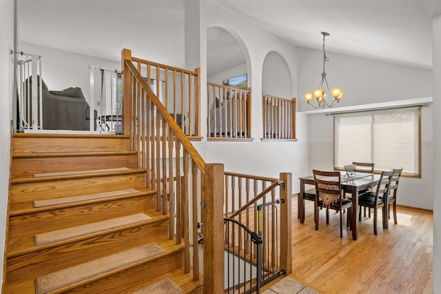 stairs featuring lofted ceiling, plenty of natural light, a chandelier, and wood finished floors