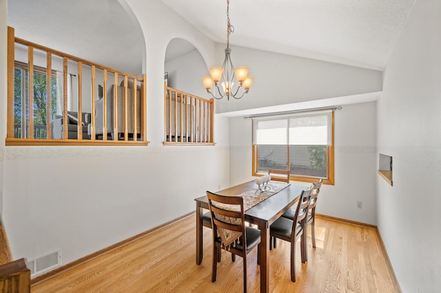 dining space featuring vaulted ceiling, wood finished floors, a chandelier, baseboards, and arched walkways