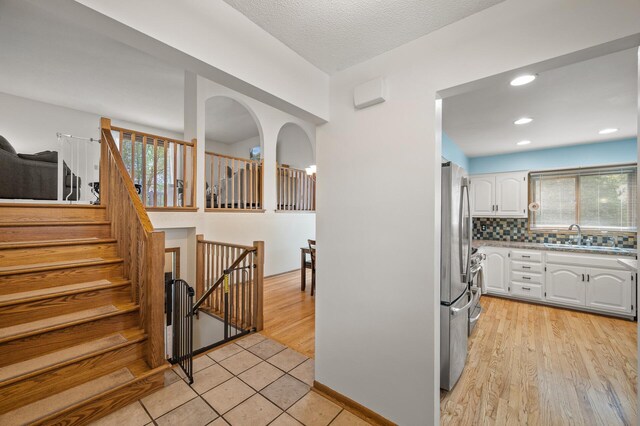kitchen with white cabinets, a sink, decorative backsplash, light wood-style floors, and freestanding refrigerator