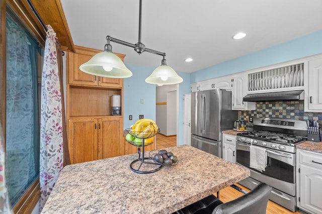 kitchen with stainless steel appliances, under cabinet range hood, decorative backsplash, white cabinets, and decorative light fixtures
