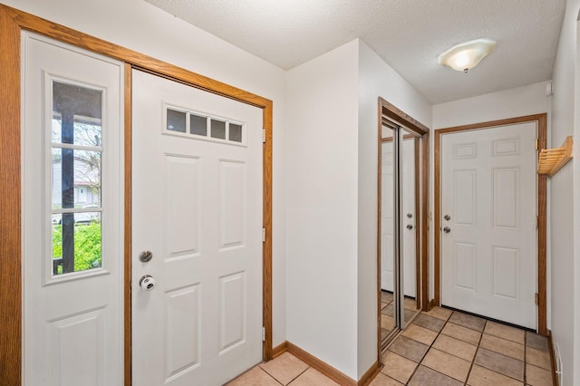 foyer featuring light tile patterned flooring, baseboards, and a textured ceiling