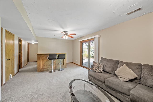living room featuring a bar, light carpet, ceiling fan, and baseboards