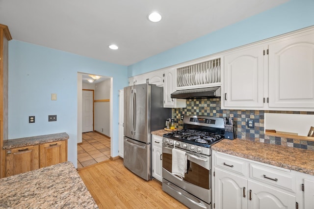 kitchen featuring appliances with stainless steel finishes, under cabinet range hood, tasteful backsplash, white cabinets, and light wood-style flooring