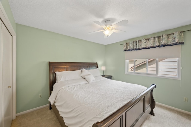 bedroom featuring light colored carpet, baseboards, a textured ceiling, a closet, and a ceiling fan
