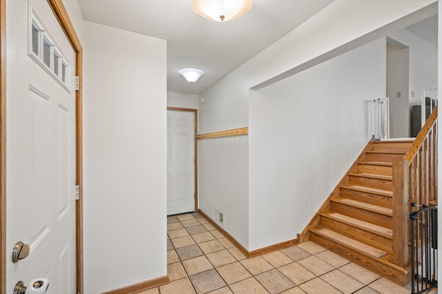 hall featuring stairway, light tile patterned floors, a textured ceiling, and baseboards