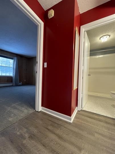 hallway with a textured ceiling, wood finished floors, and baseboards