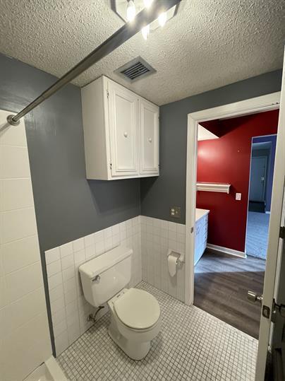 full bathroom with tile walls, toilet, a textured ceiling, wainscoting, and a shower