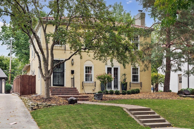 view of front facade with stucco siding, a front yard, a chimney, and a gate