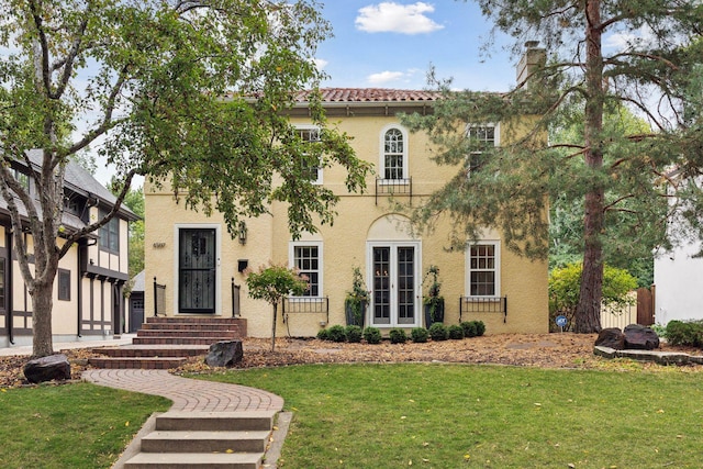 view of front of house with a front yard, stucco siding, a tiled roof, and a chimney