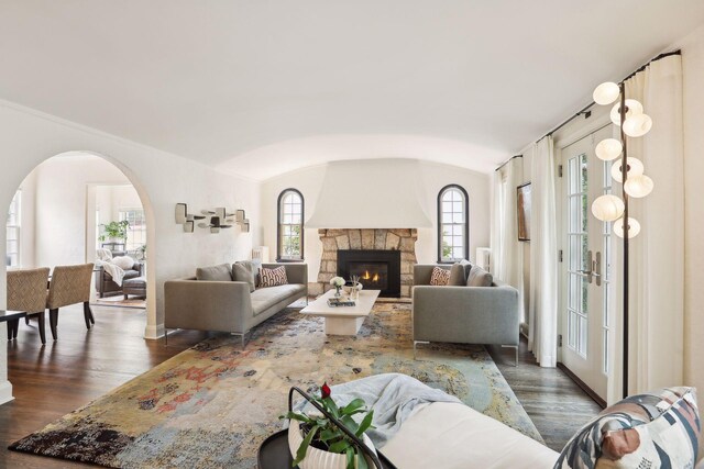 living area featuring dark wood finished floors, arched walkways, a stone fireplace, and vaulted ceiling