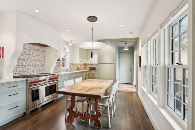 kitchen with range with two ovens, a sink, decorative backsplash, dark wood-style floors, and pendant lighting