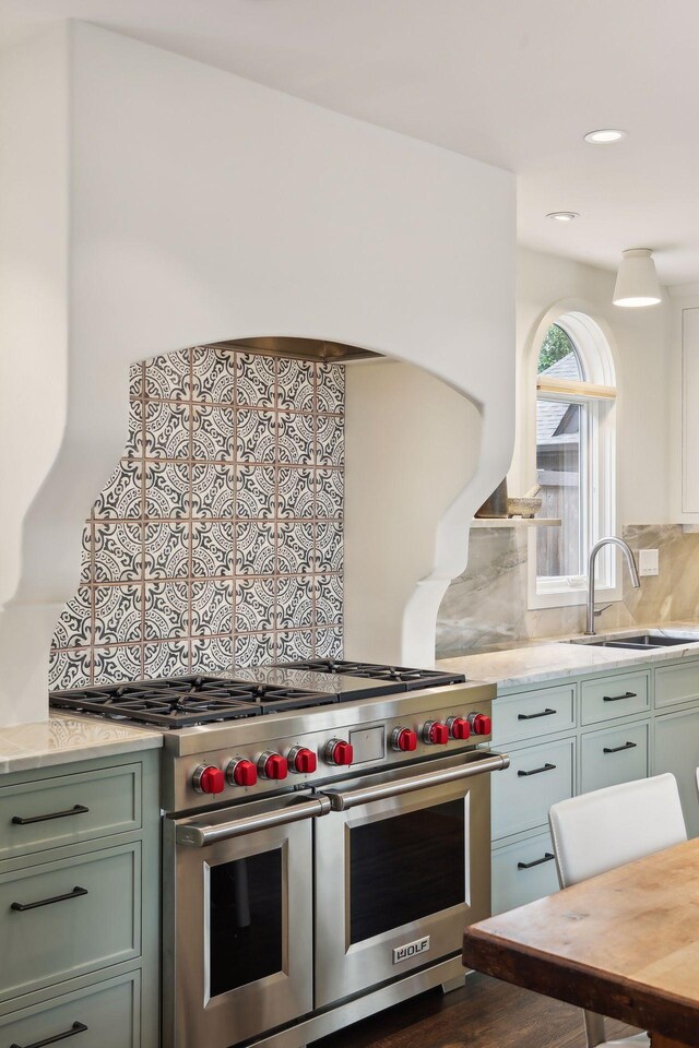kitchen featuring double oven range, tasteful backsplash, a sink, green cabinetry, and light stone counters