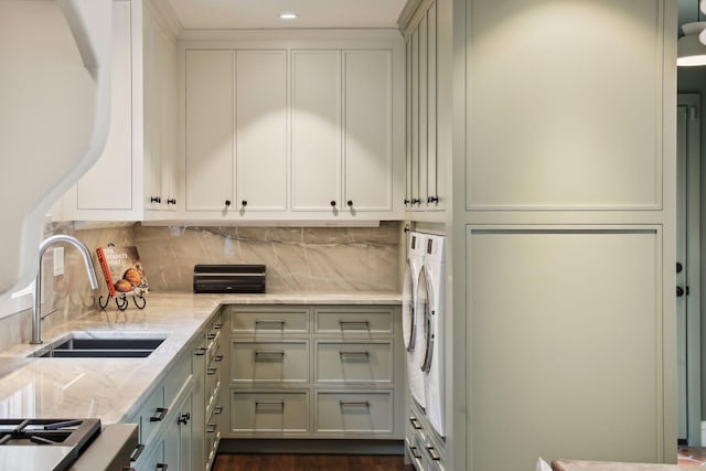 kitchen with washer and clothes dryer, a sink, light stone counters, decorative backsplash, and stove