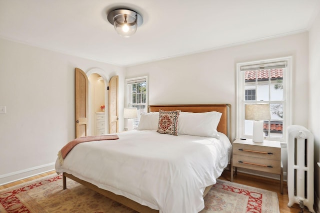 bedroom featuring radiator, wood finished floors, crown molding, and baseboards