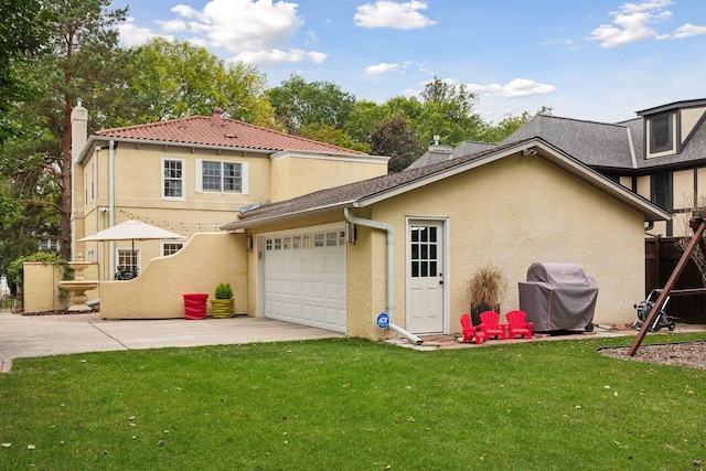 rear view of house featuring stucco siding, driveway, an attached garage, a lawn, and a chimney