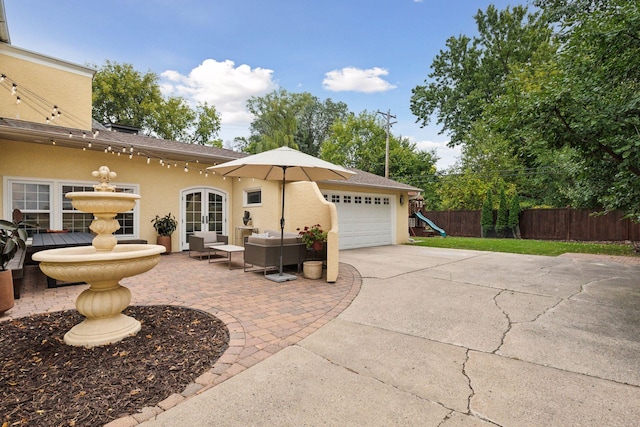 back of house featuring french doors, fence, stucco siding, driveway, and a garage