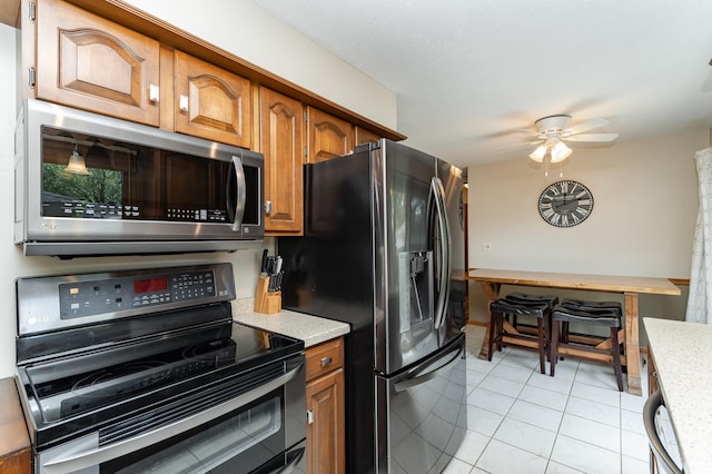 kitchen featuring stainless steel appliances, brown cabinetry, light tile patterned floors, and a ceiling fan