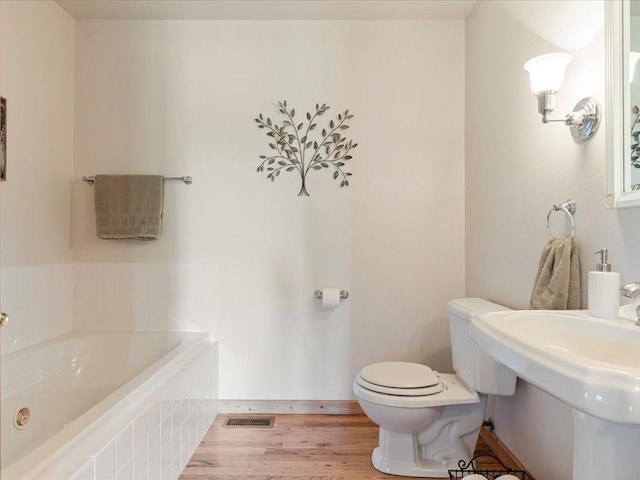 bathroom featuring a bath, toilet, a sink, and wood finished floors