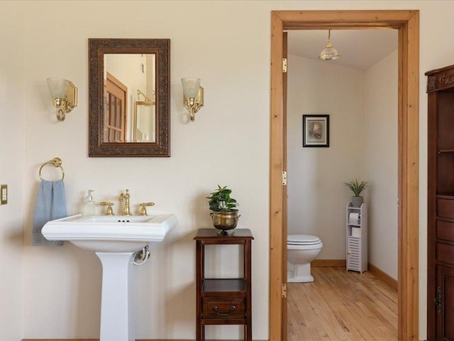 half bath with wood finished floors, toilet, a sink, and baseboards