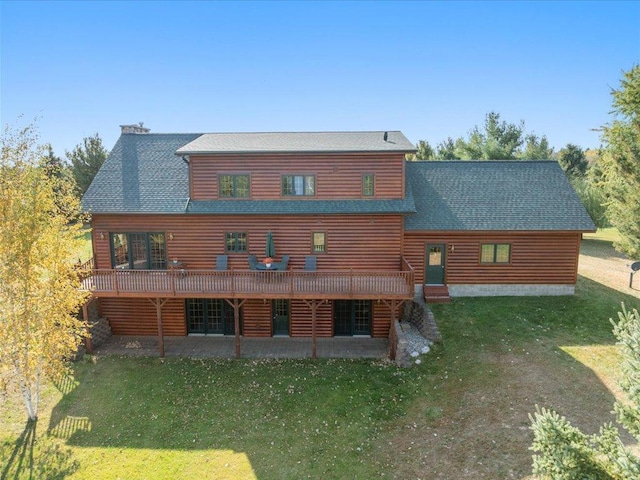 back of property featuring a lawn, a patio area, log veneer siding, a wooden deck, and a shingled roof