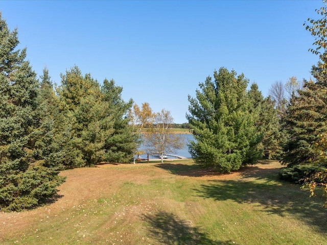 view of green lawn featuring a dock and a water view