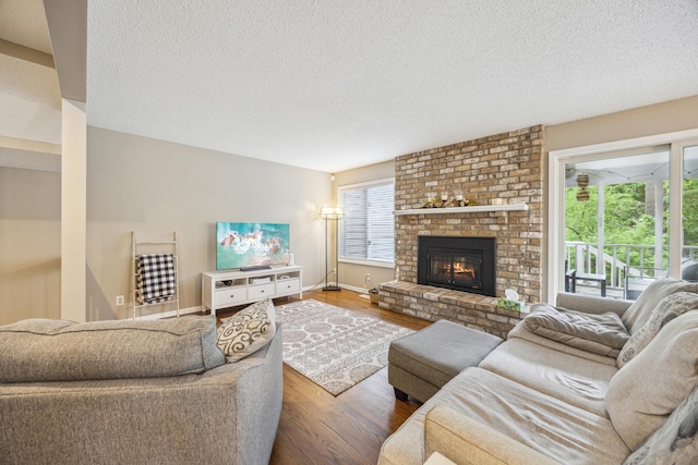 living area with wood finished floors, a textured ceiling, a brick fireplace, and baseboards