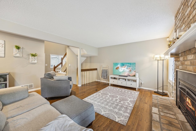 living area with a fireplace, stairs, baseboards, a textured ceiling, and wood finished floors