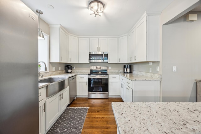 kitchen with appliances with stainless steel finishes, white cabinetry, light stone counters, dark wood-style floors, and a sink