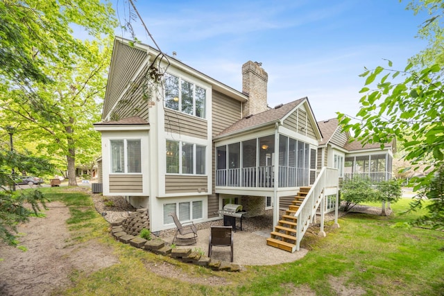 rear view of property with a sunroom, a patio area, a chimney, and a shingled roof