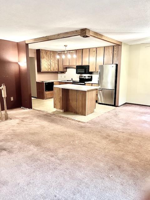 kitchen with appliances with stainless steel finishes, a kitchen island, light countertops, light carpet, and hanging light fixtures