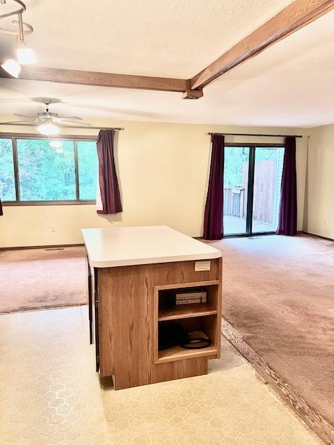 unfurnished living room with light colored carpet, beamed ceiling, a ceiling fan, and baseboards