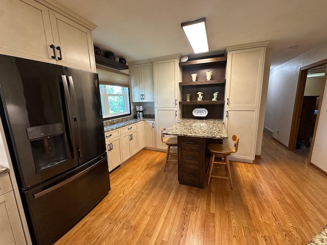 4220 23rd St NW, Willmar, MN 56201 - kitchen with black fridge, open shelves, light wood-style flooring, a kitchen bar, and light stone counters