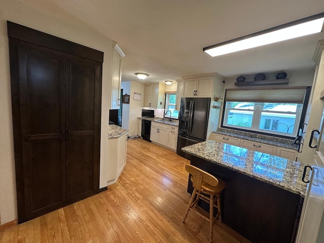 4220 23rd St NW, Willmar, MN 56201 - kitchen featuring black appliances, a sink, light wood-style floors, light stone counters, and white cabinetry