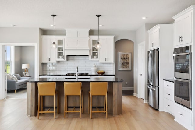 4789 131st Ct NE, Blaine, MN 55449 - kitchen featuring appliances with stainless steel finishes, decorative backsplash, light wood finished floors, a kitchen bar, and glass insert cabinets