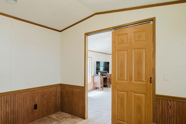 corridor featuring wainscoting, light colored carpet, vaulted ceiling, crown molding, and a desk