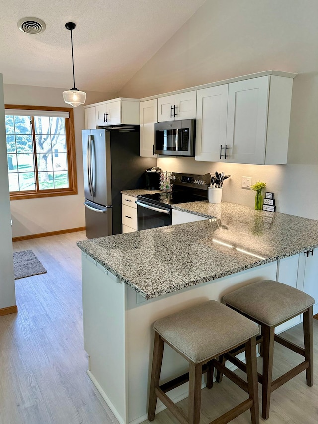 kitchen featuring stainless steel appliances, light stone counters, a peninsula, light wood-style flooring, and lofted ceiling