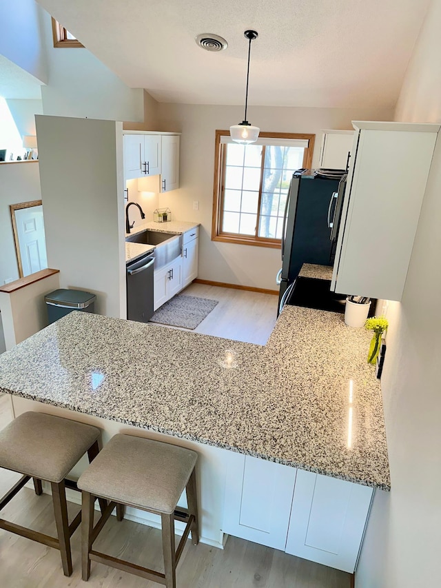 kitchen featuring a sink, stainless steel appliances, light wood-style flooring, light stone counters, and white cabinets