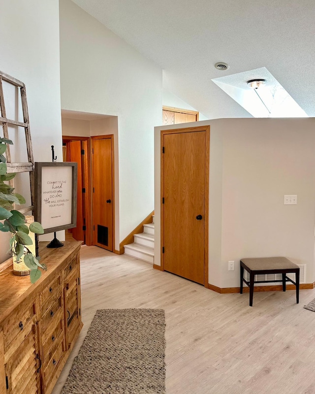 hallway featuring a skylight, vaulted ceiling, wood finished floors, stairway, and baseboards