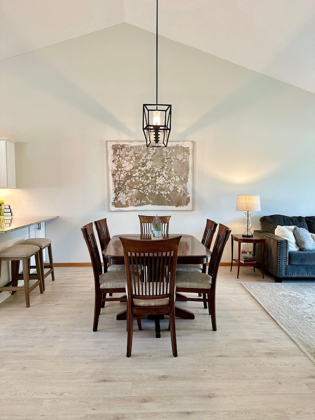 dining space with light wood-type flooring, baseboards, and high vaulted ceiling