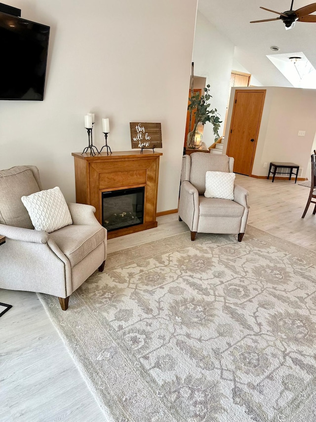 living area with a ceiling fan, wood finished floors, a glass covered fireplace, vaulted ceiling, and a skylight