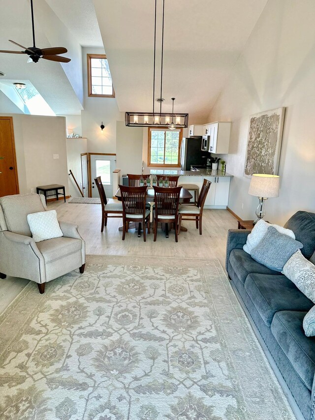 living area with high vaulted ceiling, a ceiling fan, a skylight, and baseboards