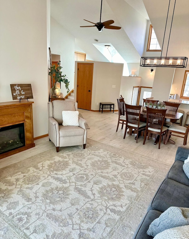 living area featuring ceiling fan, high vaulted ceiling, a skylight, a glass covered fireplace, and wood finished floors
