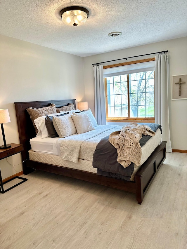 bedroom with light wood-style floors, a textured ceiling, and baseboards