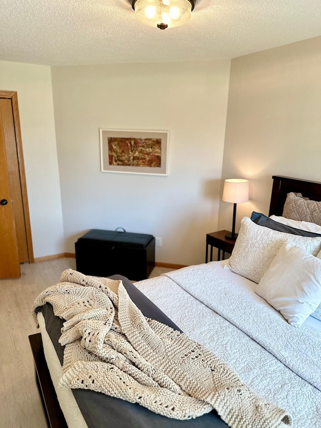 bedroom with light wood-type flooring, a textured ceiling, and baseboards