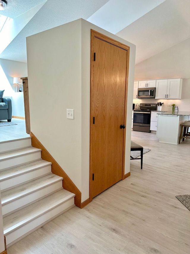 staircase featuring wood finished floors, baseboards, and lofted ceiling